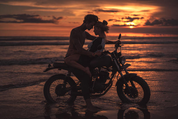 pareja apasionada abrazando y tocando con la frente en motocicleta en la playa durante el atardecer
  - Foto, Imagen