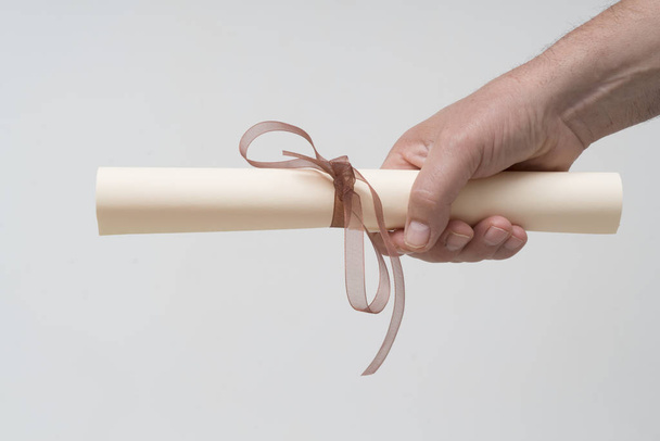 a diploma rolled up and tied with a red ribbon on the hand - 写真・画像