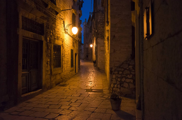 City of Sibenik Croatia Europe at night. Warm beautiful summer night with yellow and red color tones. Small alleys between houses and buildings at nice evening. Stone ground and walls - Foto, afbeelding
