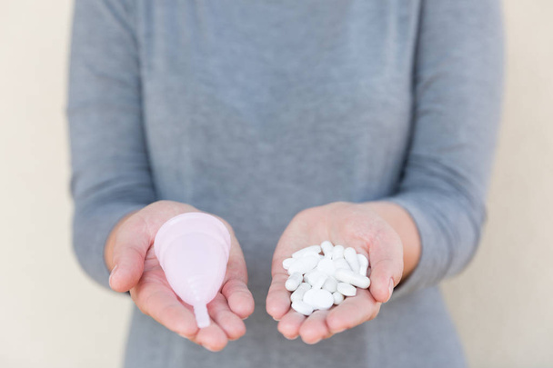 Tablets or Menstrual cup? Menstrual mug and tablets holds a female hand. - Foto, immagini