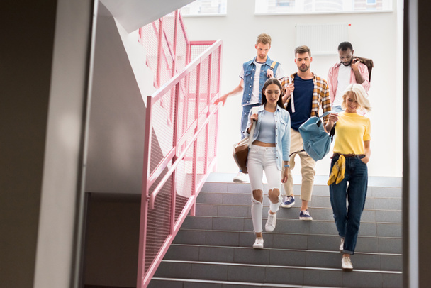 tyylikkäät nuoret opiskelijat kävelevät alas portaita college käytävällä
 - Valokuva, kuva