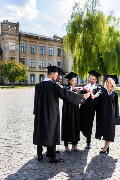 giovani studenti laureati felici fare gesto di squadra con diplomi arrotolati
 - Foto, immagini