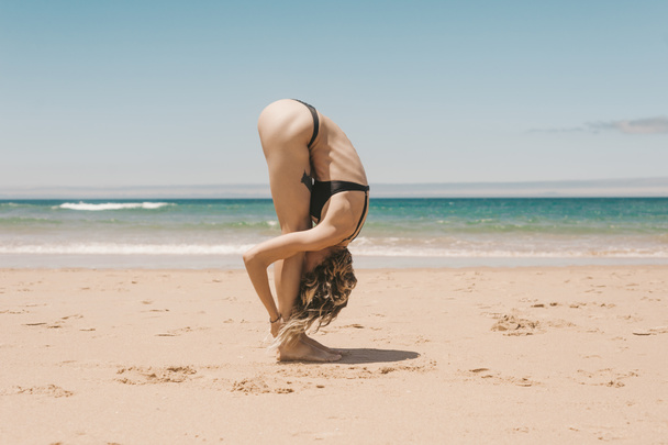 вид сбоку на молодую женщину, стоящую в позе йоги на песчаном пляже
 - Фото, изображение