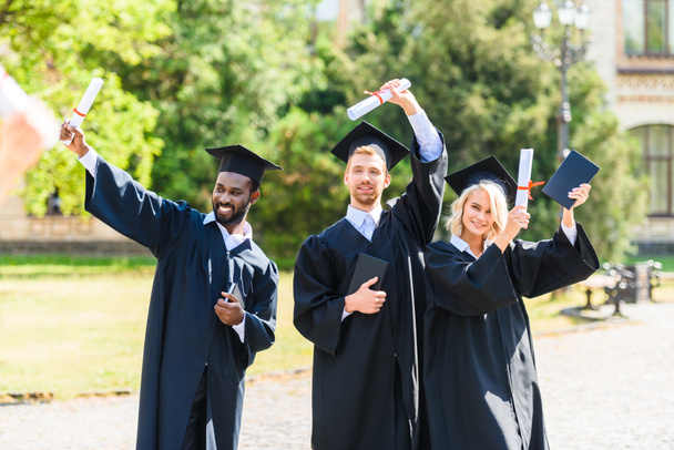 šťastný mladý absolvent studentů v pláště drží diplomy - Fotografie, Obrázek