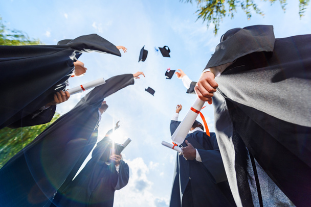vista inferior de los estudiantes graduados vomitando sombreros delante del cielo azul
 - Foto, Imagen
