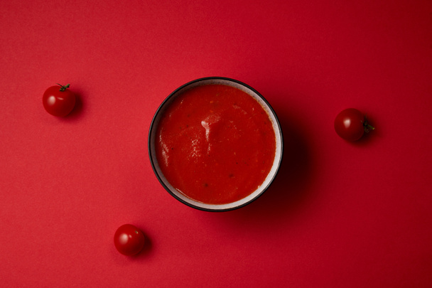 bovenaanzicht van heerlijke tomatensoep in plaat en drie verse tomaten op rode tafel - Foto, afbeelding