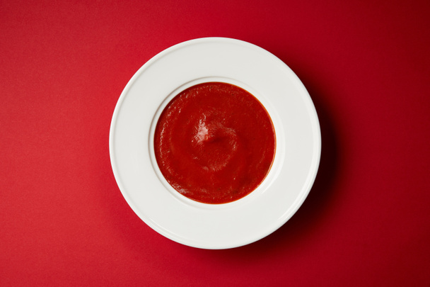 vue du dessus de la soupe de tomates savoureuse dans une assiette blanche sur la table rouge
 - Photo, image