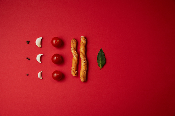 style alimentaire de tomates savoureuses, ail, bâtonnets de pain et feuille de laurier sur la table rouge
 - Photo, image