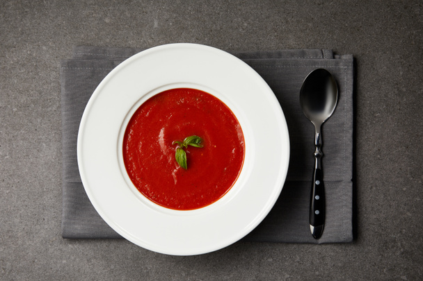 elevated view of tasty tomato soup in plate and spoon on grey napkin on grey table - Photo, Image