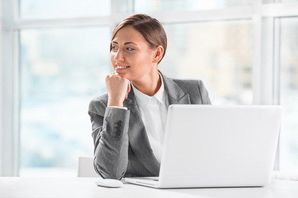 Thoughtful business woman holding chin while using laptop at wor - Photo, image