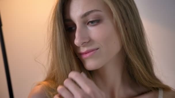 Young blonde pretty women with blue eyes looking sideways and touching her hair, smiling - Filmati, video