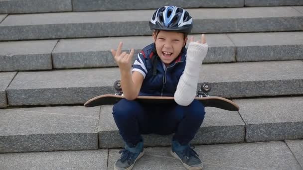 Biały chłopiec ze złamaną rękę makng znak rock - Materiał filmowy, wideo