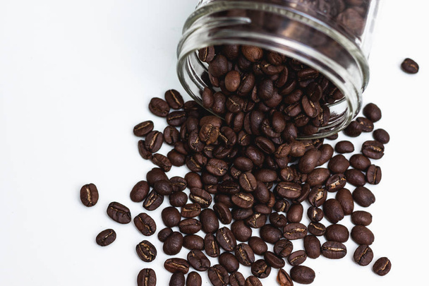 Coffee beans coming out of a glass jar on a white background - Photo, Image
