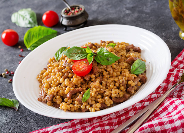 Israeli couscous with beef on white plate with napkin, fork and spoon - Photo, Image
