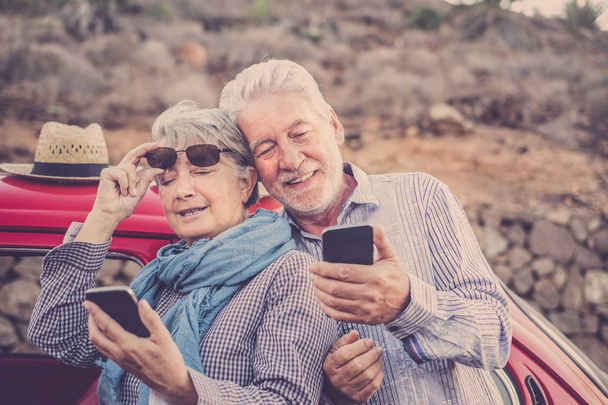 Szczęśliwa para senior starszych używać telefonów komórkowych odkryty w pobliżu czerwony piękny samochód retro. aktywny wypoczynek aktywności i podróży koncepcja razem na zawsze. nowoczesne zastosowania technologii od wiek dorosły, który cieszył się życiem - Zdjęcie, obraz