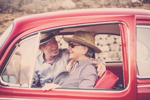 İki son sınıf erkek ve kadın için eski bir kırmızı araba, o gülümsüyor ve baktığını. Şapka ile her ikisi de. Alternatif seyahat kavramı. - Fotoğraf, Görsel