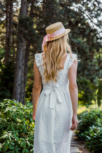 back view of attractive girl in white dress and wicker hat walking in forest - Φωτογραφία, εικόνα