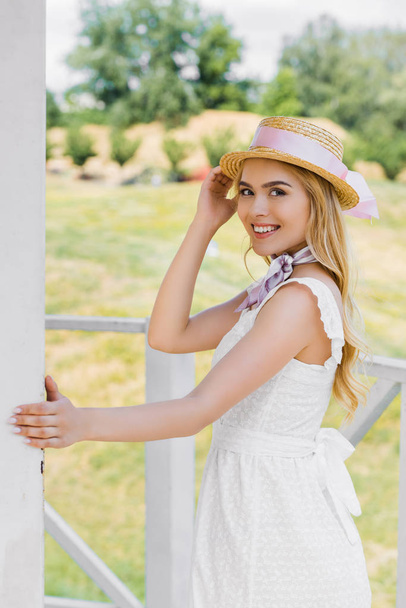 beautiful young woman in wicker hat and white dress smiling at camera - Fotoğraf, Görsel