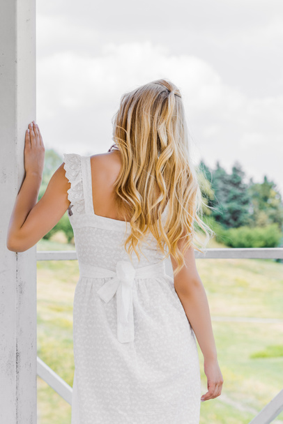 back view of beautiful blonde girl in white dress looking at green plants  - Photo, Image