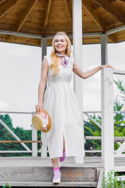 πλήρες μήκος δείτε χαρούμενος νεαρή γυναίκα σε λευκό φόρεμα βάδιση στην Σκάλα - Φωτογραφία, εικόνα