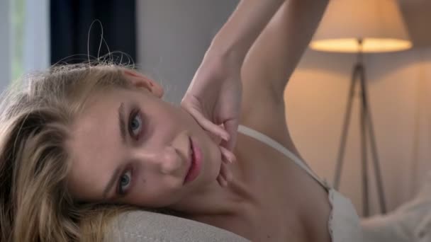 Young sexy blonde women lying on sofa and looking into camera, beauty portrait of posing model - Materiaali, video
