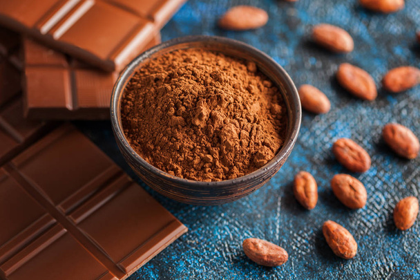 tazón con cacao en polvo y barras de chocolate con granos de cacao sobre fondo azul, concepto de comida dulce
  - Foto, Imagen