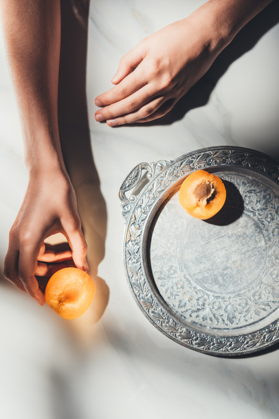 partial view of woman holding piece of apricot on light marble surface - Foto, Imagen