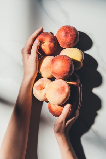 cropped shot of woman holding fresh and ripe peaches on light marble surface - Fotoğraf, Görsel