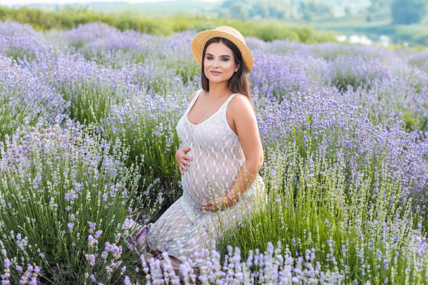 szép terhes nő fehér ruhában Ibolya levendula mező ül és nézi a kamera - Fotó, kép
