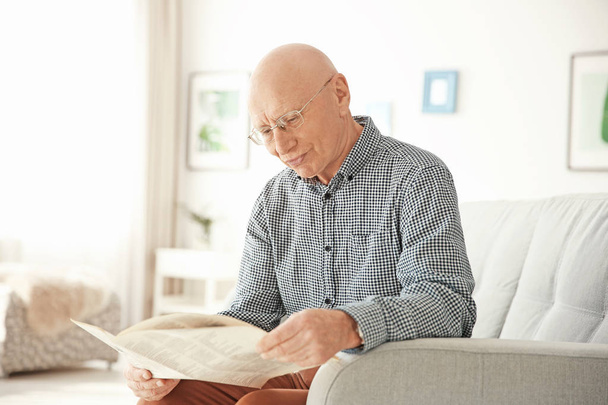Elderly man reading newspaper in living room - Fotó, kép