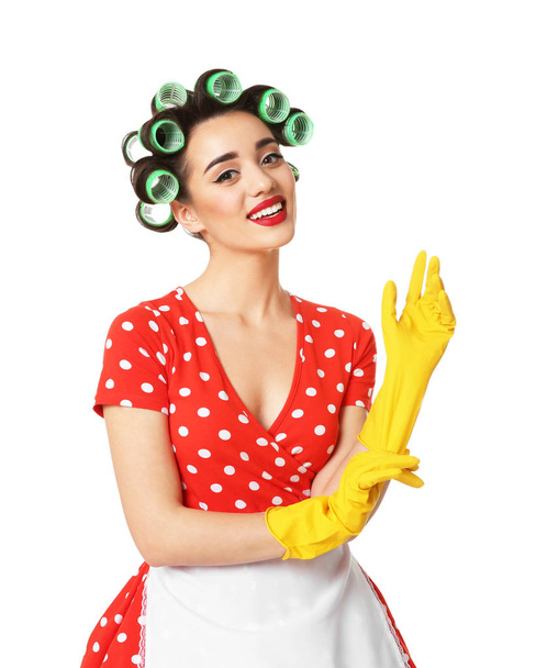 Grappige jonge huisvrouw met haar rollen rubberen handschoenen tegen witte achtergrond zetten - Foto, afbeelding