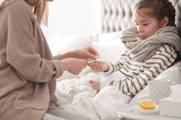 Mother giving pills to little daughter suffering from cold in bed - Fotoğraf, Görsel