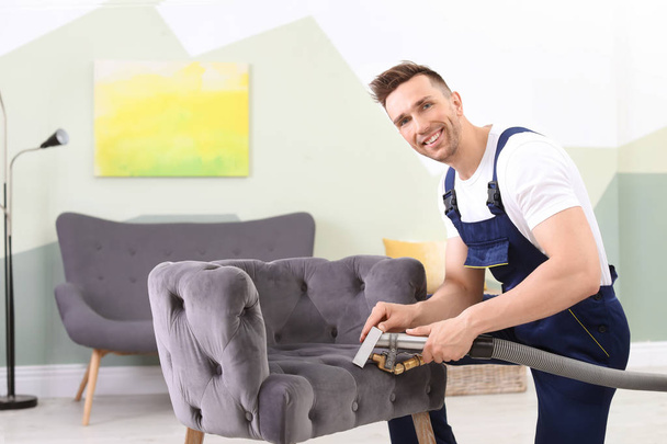 Male worker removing dirt from armchair with professional vacuum cleaner indoors - Zdjęcie, obraz