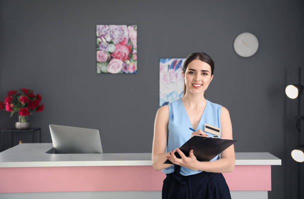 Young receptionist with clipboard at desk in beauty salon - Φωτογραφία, εικόνα