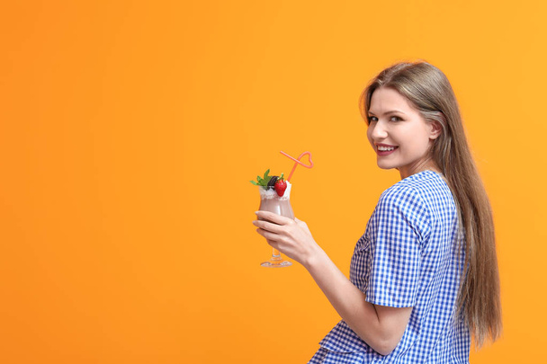 Jonge vrouw met een glas heerlijke milkshake op kleur achtergrond - Foto, afbeelding