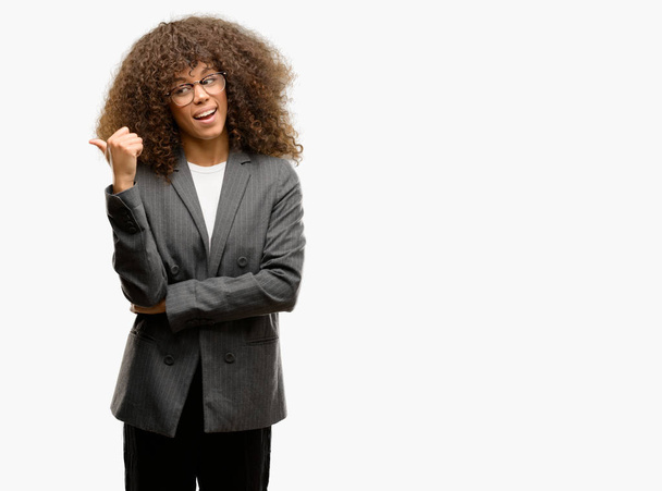 Афро-американських бізнес жінка в окулярах посміхається з щасливим обличчям, дивлячись і вказуючи на сторону з великим пальцем. - Фото, зображення