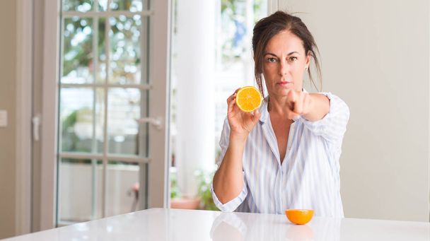 Frau mittleren Alters mit orangefarbenen Früchten, die mit dem Finger auf die Kamera und auf dich zeigen, Handzeichen, positive und selbstbewusste Geste von vorne - Foto, Bild
