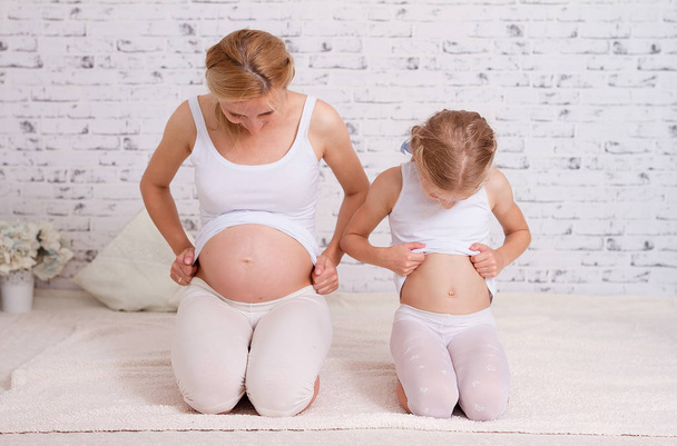 Retrato de maternidad de una madre embarazada y su hija mirando todas sus barrigas
 - Foto, imagen