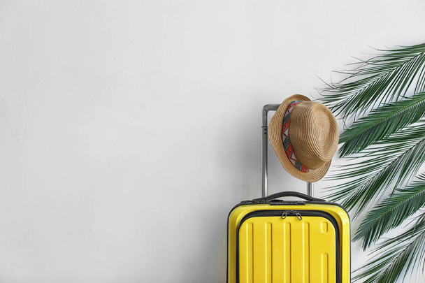 Bright yellow suitcase with hat and palm branches on light background - Foto, Imagem