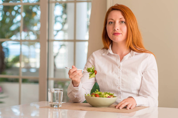Руда жінка їсть свіжий зелений салат вдома з впевненим виразом на розумне обличчя думаючи серйозно
 - Фото, зображення