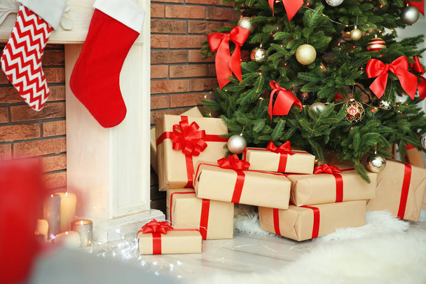 Beautiful Christmas tree and gifts near decorative fireplace with stockings indoors - Fotoğraf, Görsel