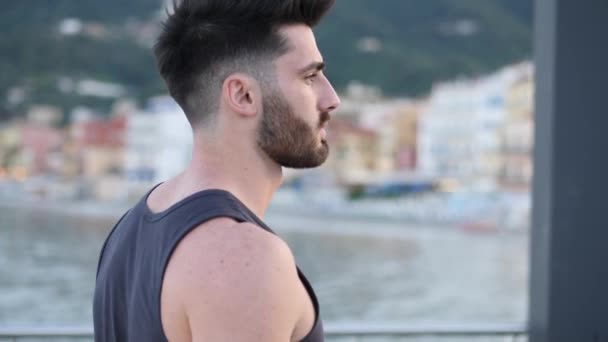 Attractive athletic young man on seaside promenade - Filmati, video