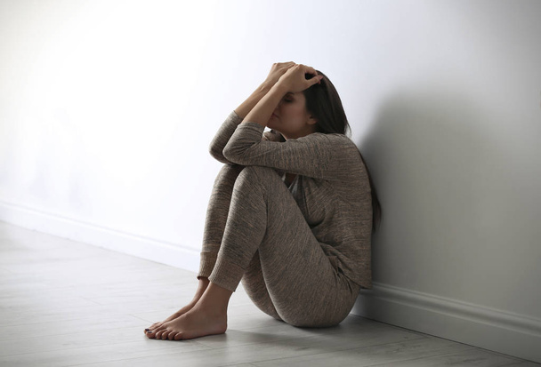 Przygnębiona młoda kobieta siedzi na podłodze w pobliżu ściana światło - Zdjęcie, obraz