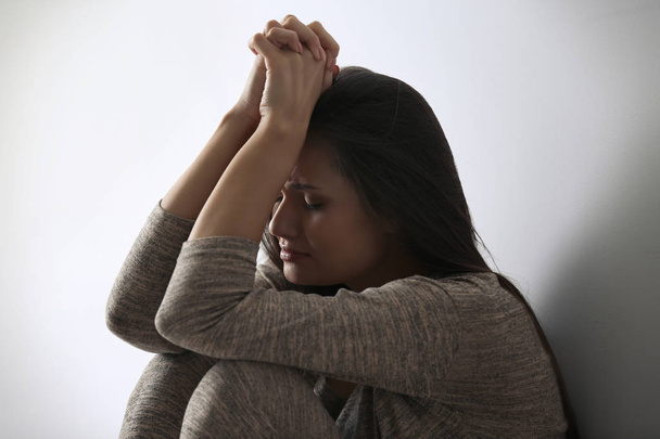 Depressed young woman sitting near light wall - Фото, зображення