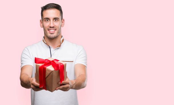 Handsome young man giving a present with a happy face standing and smiling with a confident smile showing teeth - Foto, Imagem