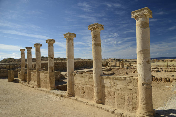 Antiguas columnas con capiteles iónicos contra el cielo azul con fondo de nubes. Pequeño mar azul es visible en el medio. Ruinas de la ciudad de Salamis, Norte de Chipre
. - Foto, imagen