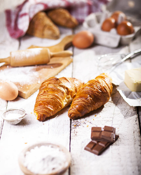 Baked croissants and ingredients for the preparation of bakery products. Rustic style. White wooden background. - Фото, зображення
