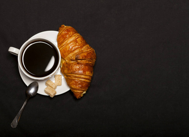 Croissant and cup of coffee on black background with copy space - Fotoğraf, Görsel