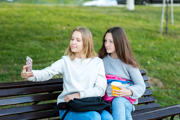 Due ragazze scolaretta. Nell'estate in parco sulla strada adolescenti. Contiene un bicchiere di caffè o tè. Fotografato al telefono. Il concetto di compagni di scuola. Foto sulla natura
. - Foto, immagini