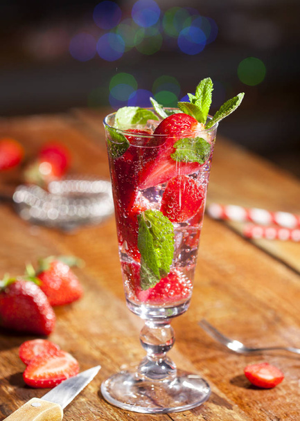 Summer cold drink with strawberries, mint and ice in glass on wooden bar counter. Closeup of cocktail with fresh berry fruits. - Fotó, kép